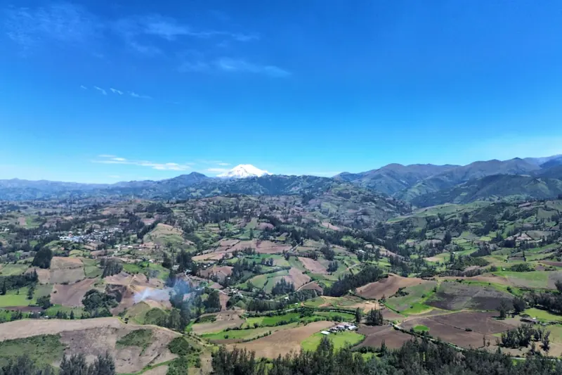 Vista aérea de un valle de la sierra con parcelas de cultivo y un volcán nevado al fondo